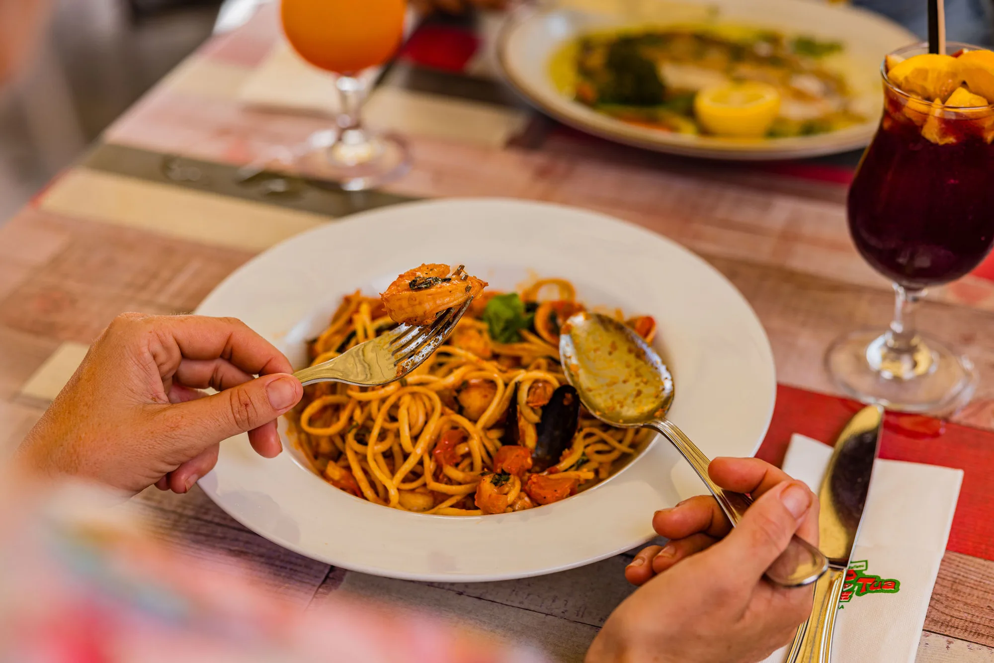 Seafood spaghetti twirled on a fork, with a glass of sangria on the table