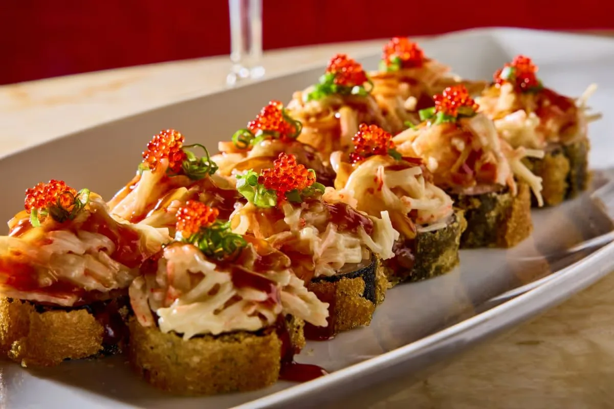 Geisha sushi rolls topped with shredded crab, red tobiko and sauce on a white plate