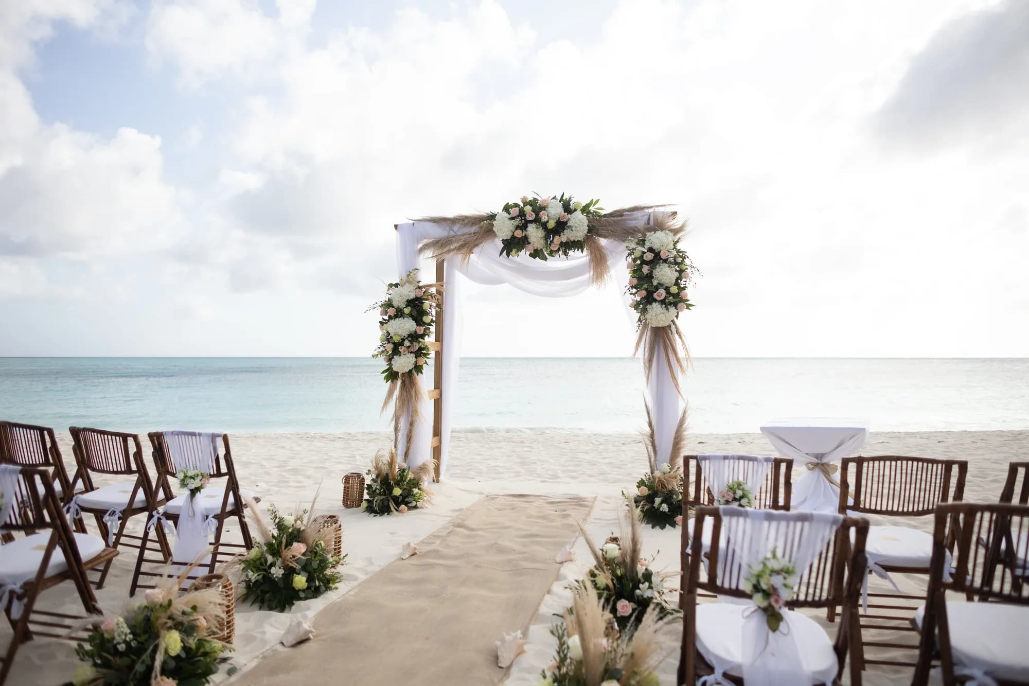 Beach ceremony setup with floral arch, aisle and chairs facing the sea