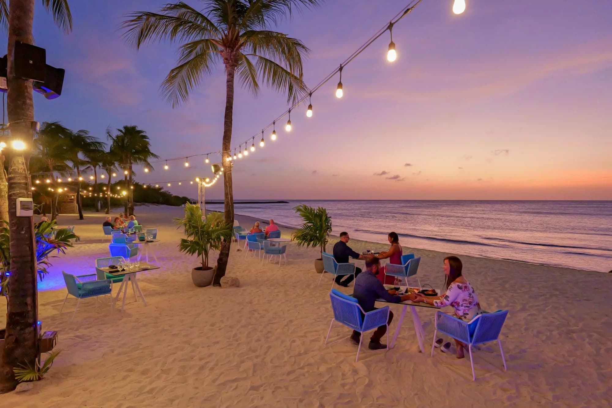 Tables on the sand under string lights at dusk